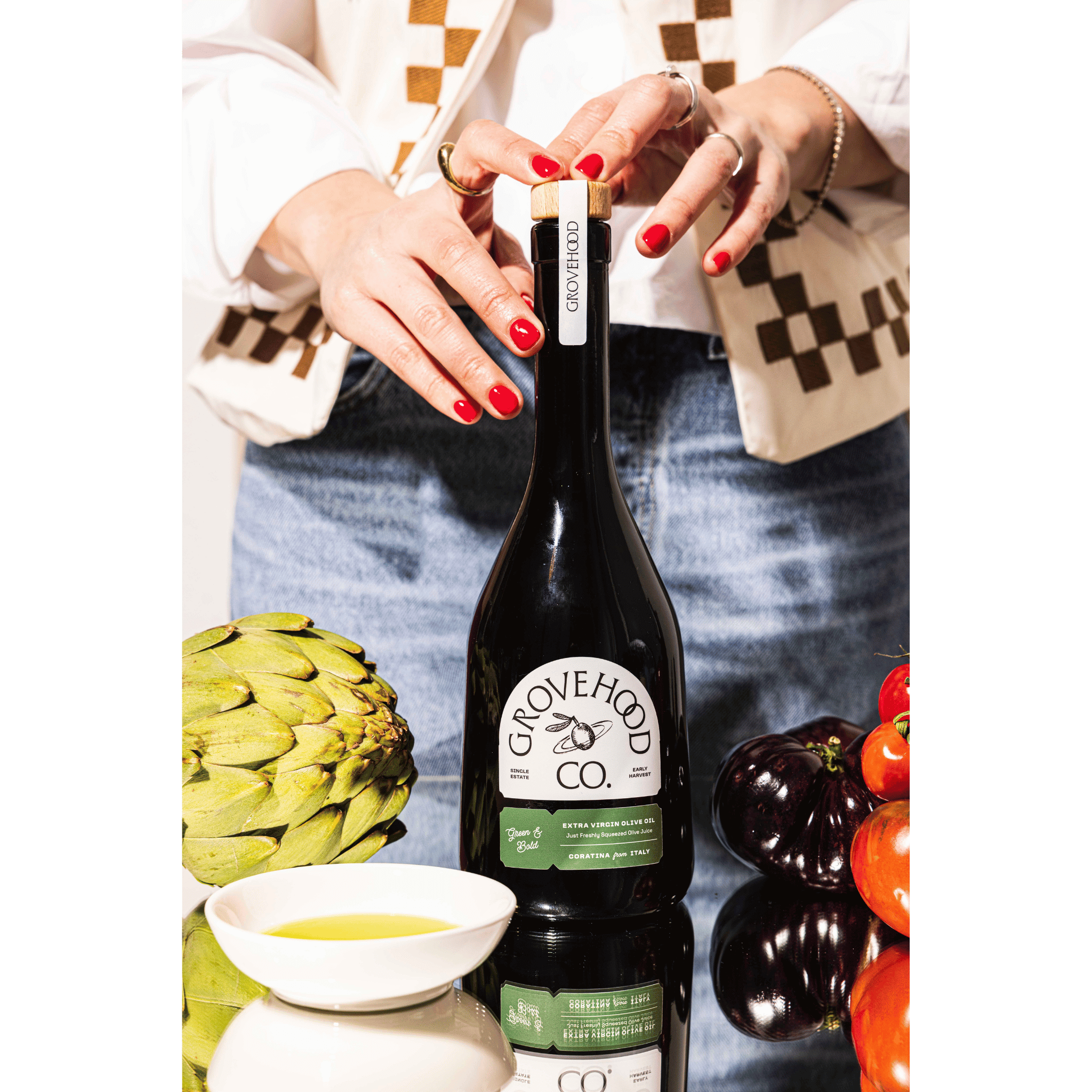 Grovehood Collective Italian extra virgin olive oil bottle at a table with tomatoes and artichoke