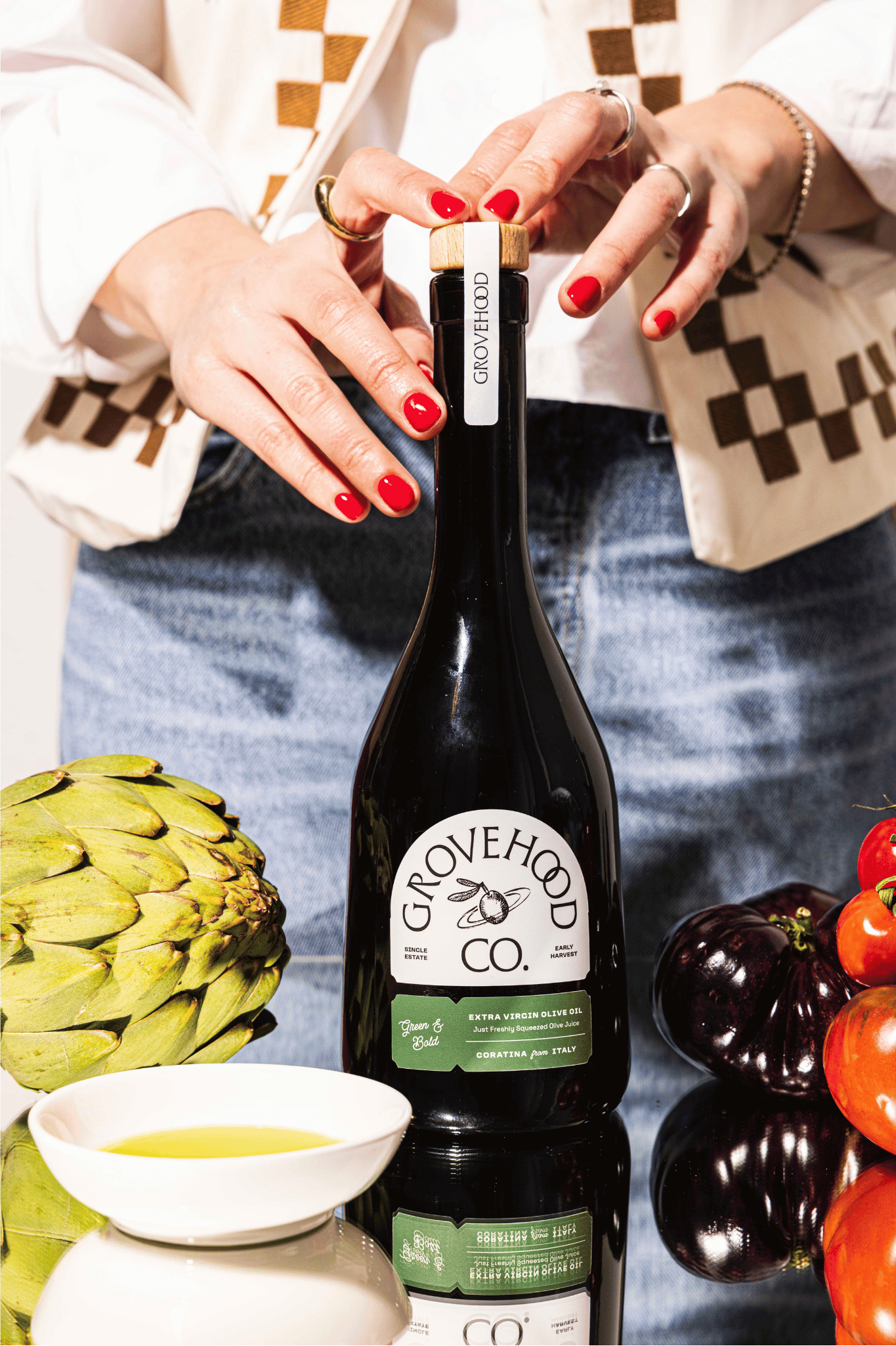 Grovehood Collective Italian extra virgin olive oil bottle at a table with tomatoes and artichoke